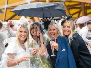 A group of race goers in rain macs holding champagne at Doncaster