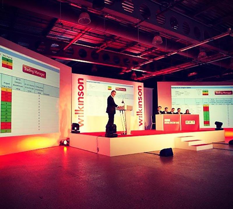 A speaker giving a talk from a raised branded platform in the exhibition hall at Doncaster Racecourse.
